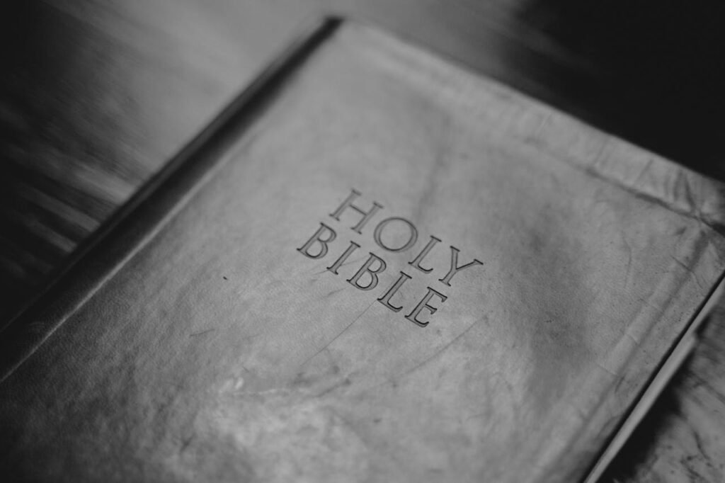 A grayscale closeup shot of the Holy Bible lying on a surface.